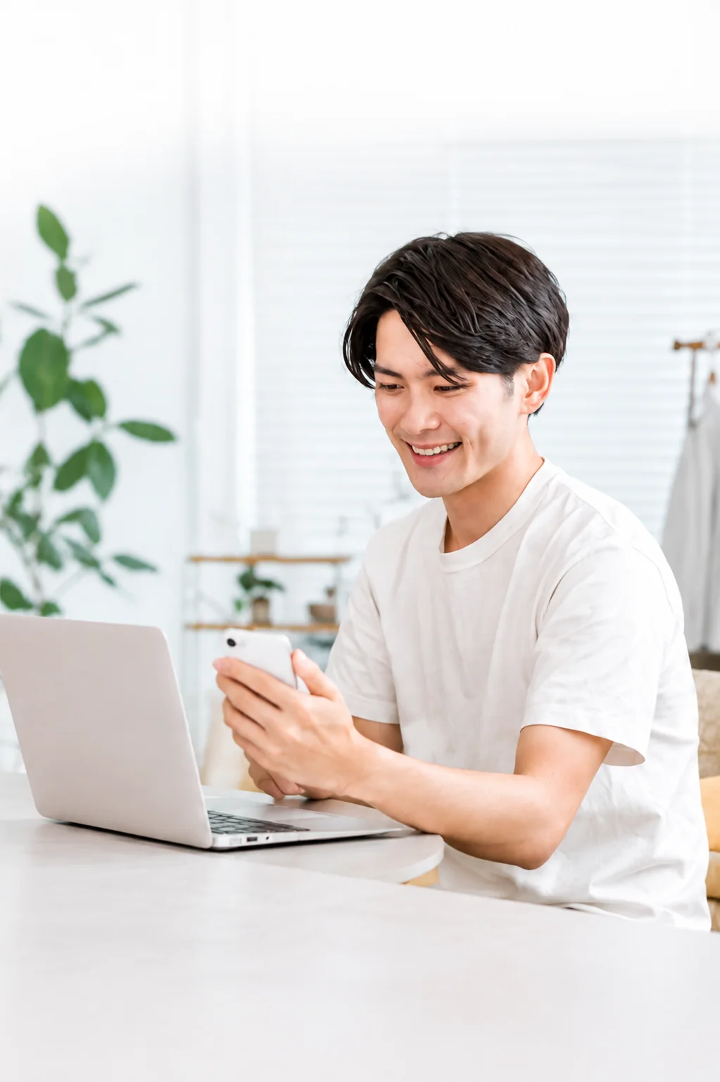 パソコンの前でスマートフォンを確認する白いシャツの男性